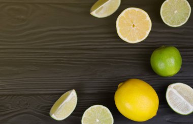 Siyah ahşap masada bir sürü sarı limon ve yeşil limon dilimleri var. Metnin için fotokopi alanı olan taze meyveler mutfakta.