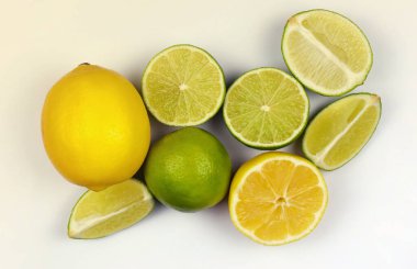 Açık beyaz masada bir sürü sarı limon ve yeşil limon dilimleri var. Mutfakta taze meyve var.