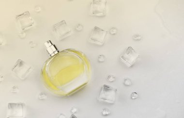 Kadın parfümü sarı şişe, buz küplerinde parfüm şişesinin objektif fotoğrafı ve beyaz masanın üzerindeki su. Yukarıdan bak. Model ürün fotoğrafı, tazelik ve aroma konsepti
