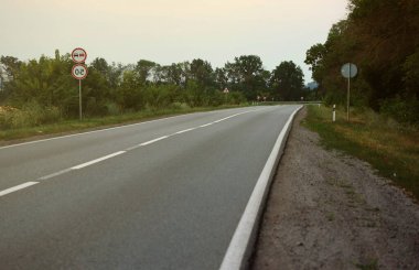 Akşam vakti boş asfalt yolu ve farklı çim ve çiçeklerden oluşan çiçek tarlası. Kenar mahalle manzarası