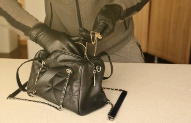 Siyah kıyafetli ve eldivenli soyguncu, çalıntı kadın çantasının içini görmüş. Hırsız mutfaktaki bir kadın çantasından altın kolyeyi çıkardı.