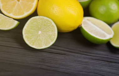 Siyah ahşap masada bir sürü sarı limon ve yeşil limon dilimleri var. Metnin için fotokopi alanı olan taze meyveler mutfakta.