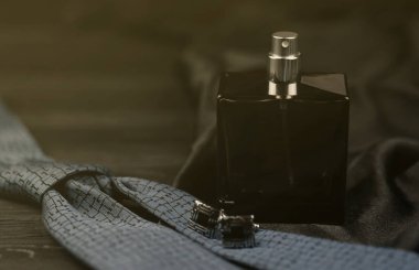 Bir şişe erkek parfümü ve mavi kravatlı kol düğmeleri ahşap bir masada siyah, lüks bir kumaş arka planda yatıyor. Erkekler klasik aksesuarlar. Sığ DOF