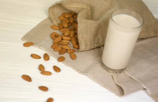 Glass of almond milk with almond nuts on canvas fabric on white wooden table. Dairy alternative milk for detox, healthy eating and diets. Selective focus