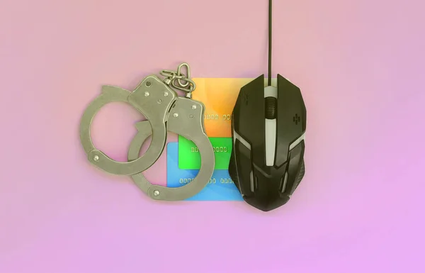 Computer mouse, credit cards and police handcuffs are on a pastel purple background. Credit card fraud concept. Carding problems