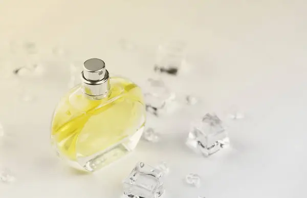 Female perfume yellow bottle, Objective photograph of perfume bottle in ice cubes and water on white table. View from above. Mockup product photo, concept of freshness.