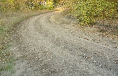Kıvrımlı bir yolu olan sonbahar manzarası üzerinde tarımsal makinelerin büyük tekerleklerinin izleri görülebilir.