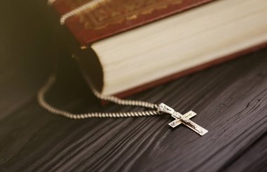 Üzerinde haç olan gümüş kolye siyah ahşap masadaki kutsal Hristiyan kitabının üzerinde. Kutsallığın gücüyle Tanrı 'dan dua etmek, şans getirir ve affedicidir..