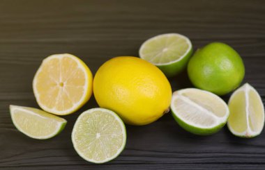 Siyah ahşap masada bir sürü sarı limon ve yeşil limon dilimleri var. Metnin için fotokopi alanı olan taze meyveler mutfakta.