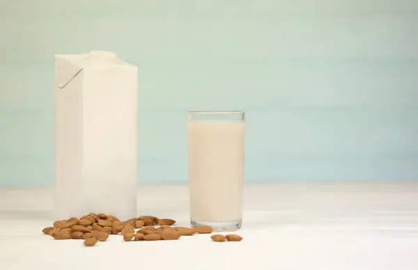 Glass of almond milk with almond nuts on canvas fabric on white wooden table. Dairy alternative milk for detox, healthy eating and diets. Selective focus