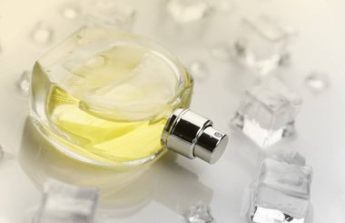 Kadın parfümü sarı şişe, buz küplerinde parfüm şişesinin objektif fotoğrafı ve beyaz masanın üzerindeki su. Yukarıdan bak. Model ürün fotoğrafı, tazelik ve aroma konsepti