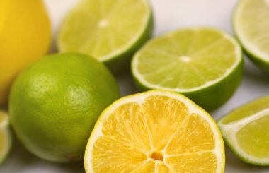 Açık beyaz masada bir sürü sarı limon ve yeşil limon dilimleri var. Mutfakta taze meyve var.