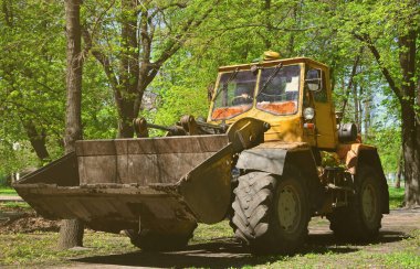 Şehir geliştirme ekibi bir ekskavatör ve bir kamyon ile parkta düşen yapraklar kaldırır. Eğlence için halka açık yerlerde geliştirmeye yönelik düzenli mevsimlik çalışma