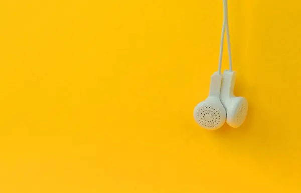 White modern headphones hanging on a bright orange background. A template for music listening fans