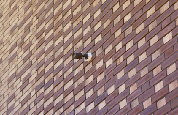Black wireless CCTV security camera for area surveillance placed on brick wall. Surveillance cameras are modern technology to prevent thieves and that are installed on red brick construction