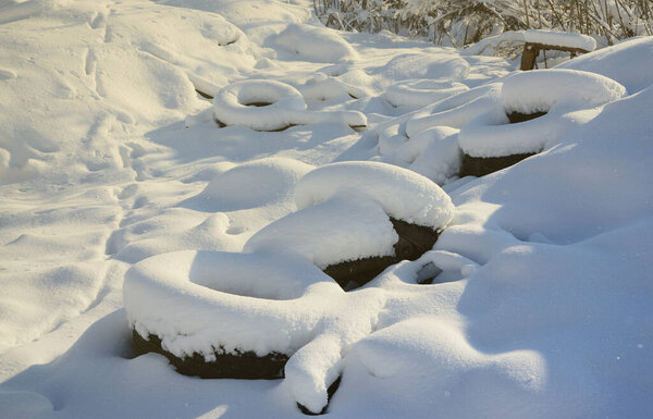 Used and discarded car tires lie on the side of the road, covered with a thick layer of snow