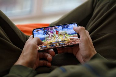 Kader, iPhone 15 akıllı telefon ekranındaki iOS mobil oyun sırasında erkeklerin elinde. Taşınabilir aygıtta mobil oyun ve eğlence
