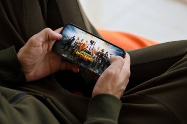 PUBG Bilinmeyen Oyuncular Battleground mobil iOS oyunu iPhone 15 akıllı telefon ekranında cep telefonu oyunu sırasında erkeklerin elinde. Taşınabilir aygıtta mobil oyun ve eğlence