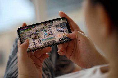 Mobil oyun sırasında iPhone 15 akıllı telefon ekranındaki M-Mobil iOS oyunu kadınların elinde. Taşınabilir aygıtta mobil oyun ve eğlence
