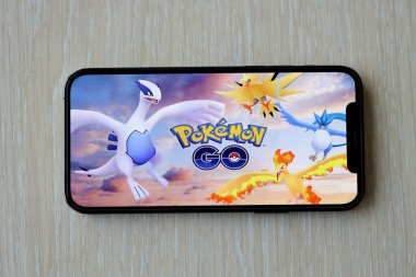 Pokemon GO mobil iOS oyunu iPhone 15 akıllı telefon ekranında ahşap masadaki mobil oyun sırasında. Taşınabilir aygıtta mobil oyun ve eğlence