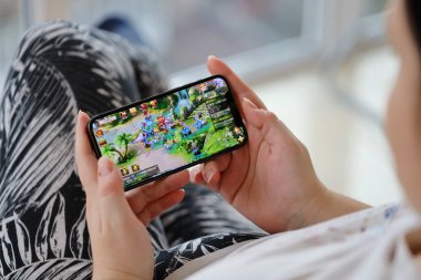 Fantezi Westward Journey mobil iOS oyunu iPhone 15 akıllı telefon ekranında mobil oyun sırasında kadınların elinde. Taşınabilir aygıtta mobil oyun ve eğlence