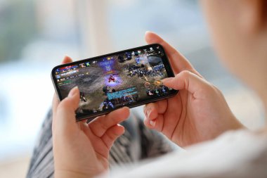 Mobil oyun sırasında iPhone 15 akıllı telefon ekranındaki M-Mobil iOS oyunu kadınların elinde. Taşınabilir aygıtta mobil oyun ve eğlence