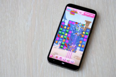Candy Crush Saga mobil iOS oyunu iPhone 15 akıllı telefon ekranında ahşap masadaki mobil oyun sırasında. Taşınabilir aygıtta mobil oyun ve eğlence