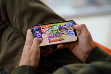 Mobil oyun sırasında iPhone 15 akıllı telefon ekranında bulmaca ve ejderhaların mobil iOS oyunu. Taşınabilir aygıtta mobil oyun ve eğlence