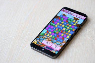 Candy Crush Saga mobil iOS oyunu iPhone 15 akıllı telefon ekranında ahşap masadaki mobil oyun sırasında. Taşınabilir aygıtta mobil oyun ve eğlence
