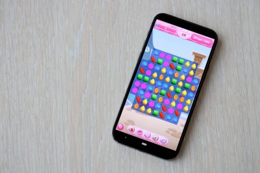 Candy Crush Saga mobil iOS oyunu iPhone 15 akıllı telefon ekranında ahşap masadaki mobil oyun sırasında. Taşınabilir aygıtta mobil oyun ve eğlence