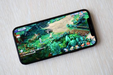 Fantezi Westward Journey mobil iOS oyunu iPhone 15 akıllı telefon ekranında ahşap masadaki mobil oyun sırasında. Taşınabilir aygıtta mobil oyun ve eğlence