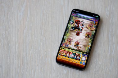 Monster Strike mobil iOS oyunu iPhone 15 akıllı telefon ekranında ahşap masadaki mobil oyun sırasında. Taşınabilir aygıtta mobil oyun ve eğlence