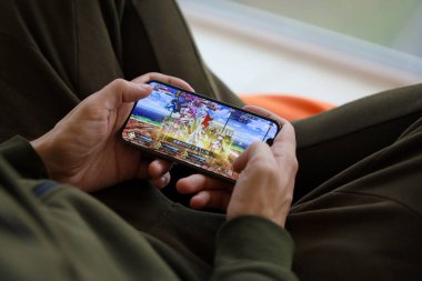 Kader, iPhone 15 akıllı telefon ekranındaki iOS mobil oyun sırasında erkeklerin elinde. Taşınabilir aygıtta mobil oyun ve eğlence