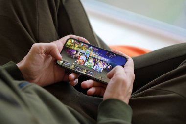 Kader, iPhone 15 akıllı telefon ekranındaki iOS mobil oyun sırasında erkeklerin elinde. Taşınabilir aygıtta mobil oyun ve eğlence