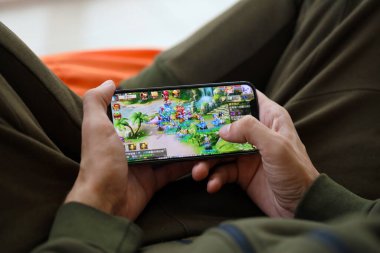 Fantezi Westward Journey mobil iOS oyunu iPhone 15 akıllı telefon ekranında cep telefonu oyunu sırasında erkeklerin elinde. Taşınabilir aygıtta mobil oyun ve eğlence