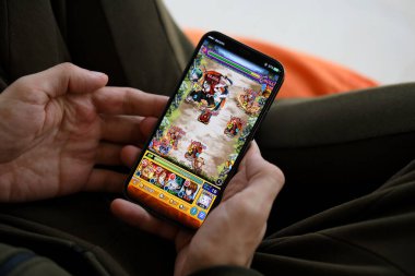 Monster Strike mobil iOS oyunu iPhone 15 akıllı telefon ekranında, oyun sırasında erkeklerin elinde. Taşınabilir aygıtta mobil oyun ve eğlence