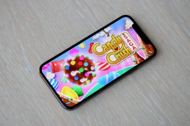 Candy Crush Saga mobil iOS oyunu iPhone 15 akıllı telefon ekranında ahşap masadaki mobil oyun sırasında. Taşınabilir aygıtta mobil oyun ve eğlence