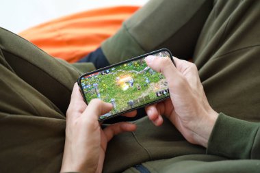 Mobil oyun sırasında iPhone 15 akıllı telefon ekranındaki M-Mobil iOS oyunu erkeklerin elinde. Taşınabilir aygıtta mobil oyun ve eğlence