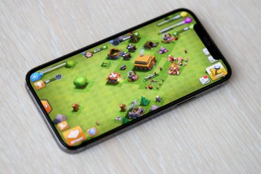 Clash of Clans mobil iOS oyunu iPhone 15 akıllı telefon ekranında ahşap masadaki mobil oyun sırasında. Taşınabilir aygıtta mobil oyun ve eğlence