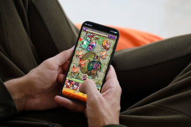 Monster Strike mobil iOS oyunu iPhone 15 akıllı telefon ekranında, oyun sırasında erkeklerin elinde. Taşınabilir aygıtta mobil oyun ve eğlence