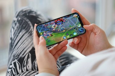 Mobil oyun sırasında iPhone 15 akıllı telefon ekranında kadınların elinde Kings 'in mobil iOS oyununun onuru. Taşınabilir aygıtta mobil oyun ve eğlence