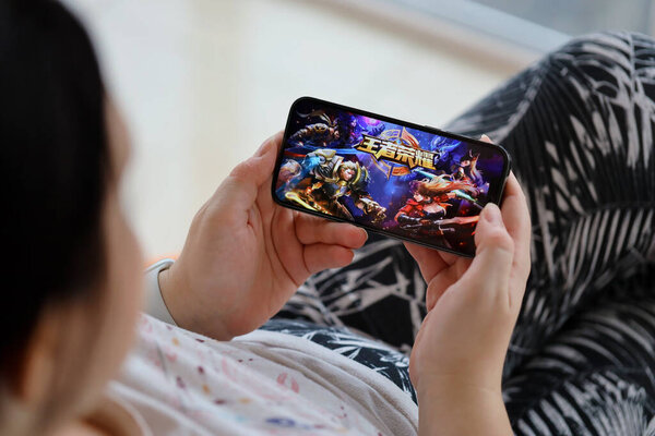 Honor of Kings mobile iOS game on iPhone 15 smartphone screen in female hands during mobile gameplay. Mobile gaming and entertainment on portable device