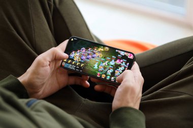 Fantezi Westward Journey mobil iOS oyunu iPhone 15 akıllı telefon ekranında cep telefonu oyunu sırasında erkeklerin elinde. Taşınabilir aygıtta mobil oyun ve eğlence