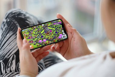 Clash of Clans mobil iOS oyunu iPhone 15 akıllı telefon ekranında mobil oyun sırasında kadınların elinde. Taşınabilir aygıtta mobil oyun ve eğlence