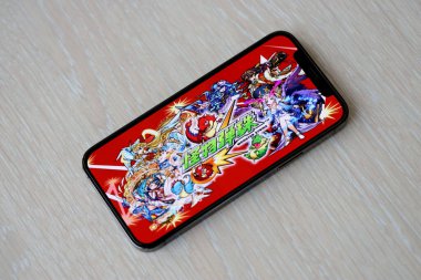 Monster Strike mobil iOS oyunu iPhone 15 akıllı telefon ekranında ahşap masadaki mobil oyun sırasında. Taşınabilir aygıtta mobil oyun ve eğlence