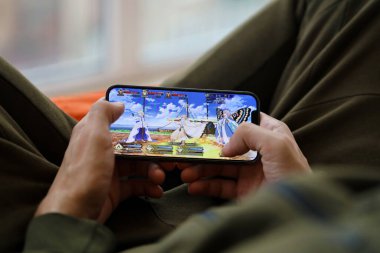 Kader, iPhone 15 akıllı telefon ekranındaki iOS mobil oyun sırasında erkeklerin elinde. Taşınabilir aygıtta mobil oyun ve eğlence