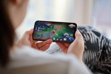 Mobil oyun sırasında iPhone 15 akıllı telefon ekranında kadınların elinde Kings 'in mobil iOS oyununun onuru. Taşınabilir aygıtta mobil oyun ve eğlence