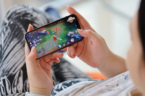 Honor of Kings mobile iOS game on iPhone 15 smartphone screen in female hands during mobile gameplay. Mobile gaming and entertainment on portable device