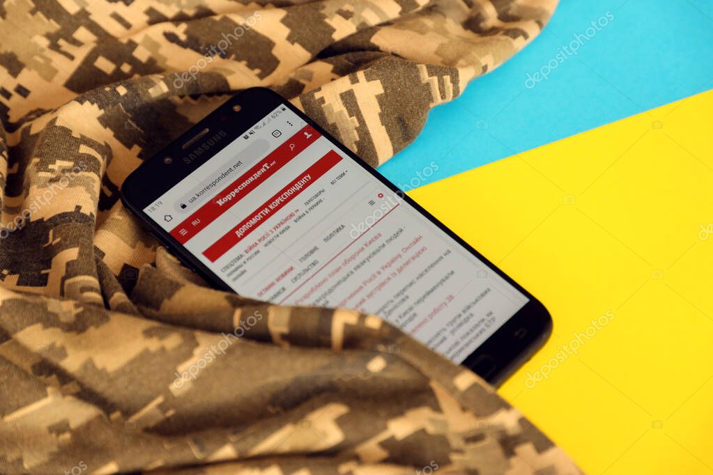 KYIV, UKRAINE - 4 MAY, 2023: Correspondent ukrainian news portal on smartphone screen with ukrainian flag and camouflage fabric close up
