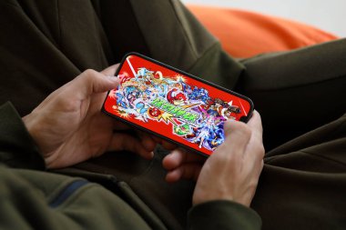 Monster Strike mobil iOS oyunu iPhone 15 akıllı telefon ekranında, oyun sırasında erkeklerin elinde. Taşınabilir aygıtta mobil oyun ve eğlence